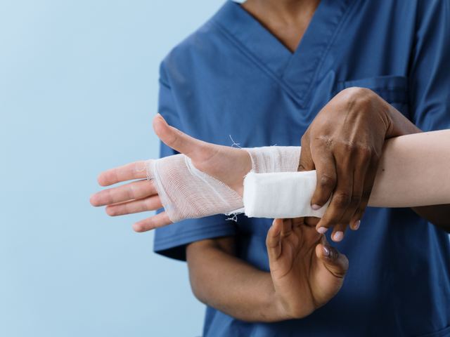 A nurse wrapping a fresh gauze dressing around a patient’s wrist and hand.