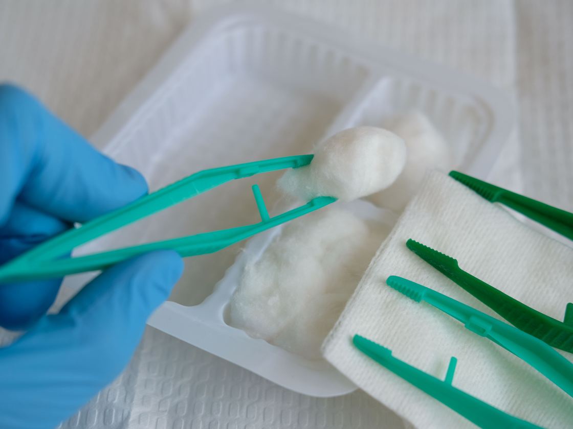 Sterile forceps lifting a cotton swab from a dressing tray.